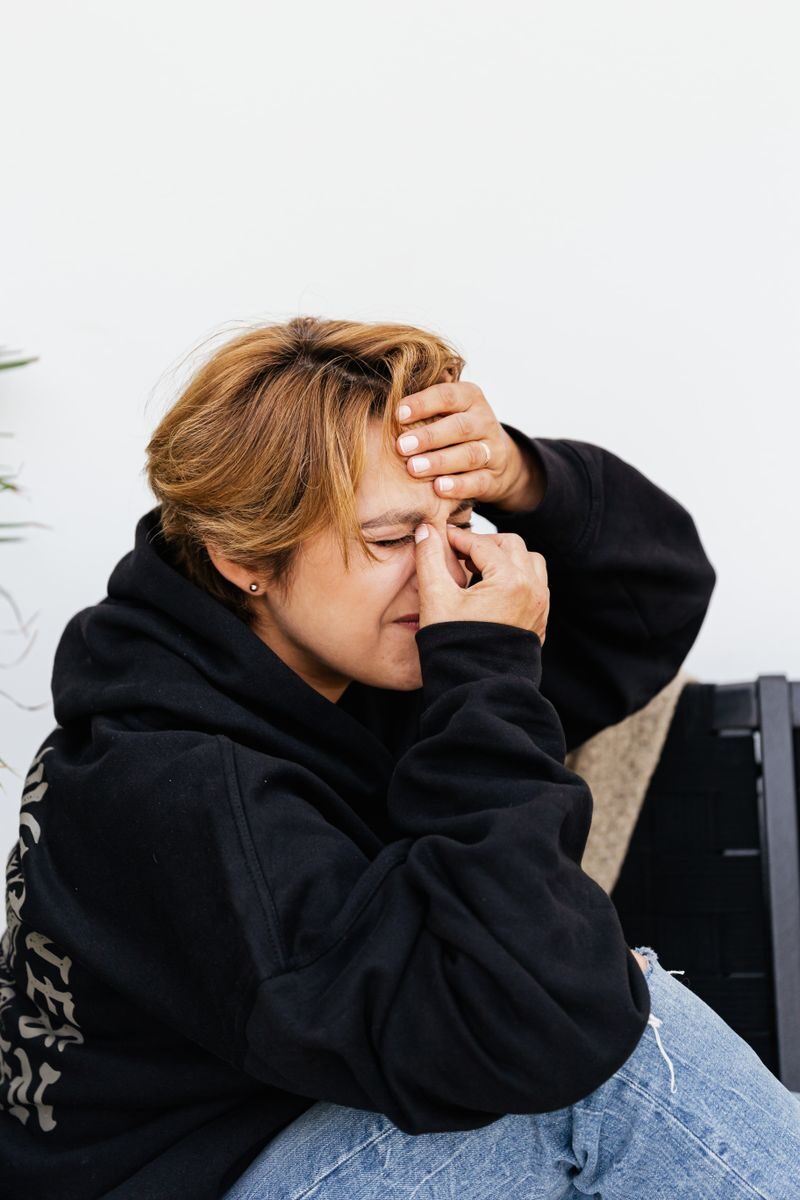 A woman in casual wear holds her head as if in pain, possibly indicating a headache or stress.
