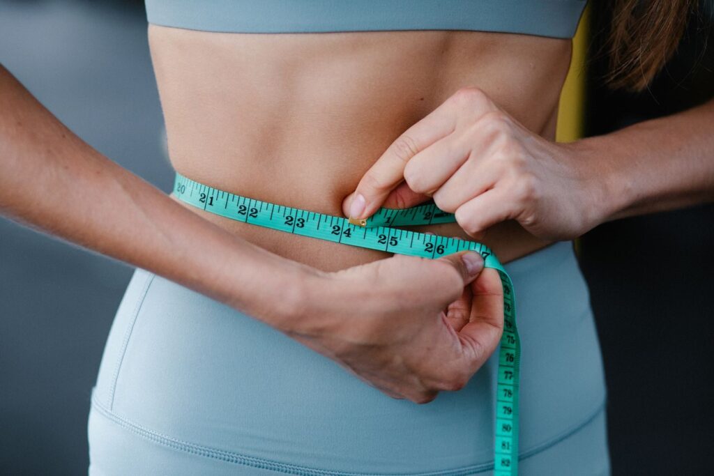 Photo by Annushka Ahuja Close-up of a woman measuring her waist with a tape, representing fitness, health, and weight loss.